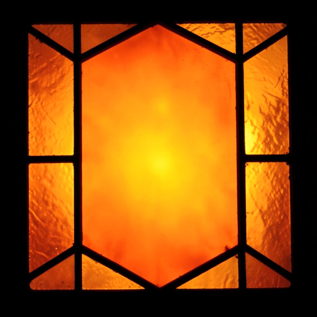A warm-toned square book cover image in ochre and deep teal, its surface divided into bold leaded stained-glass-like segments